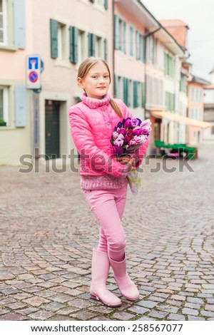 Spring portrait of adorable little girl of 7 years old, wearing bright pink coat, holding beautiful bouquet of tulips