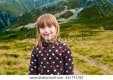 Close up portrait of a cute little girl hiking in mountains, wearing warm fleece jacket