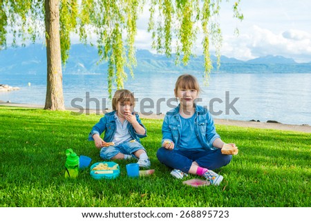Two cute kids, little girl and her brother, having a picnic outdoors by the lake