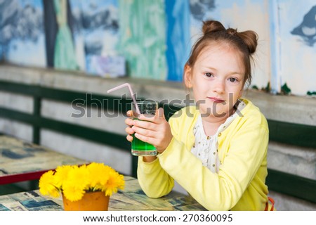 Adorable little girl drinking mint syrup in a cafe, wearing yellow jacket.