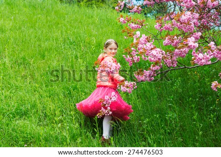 Little girl playing with a japanese cherry tree in blossom dressed in a beautiful pink tutu skirt and a shiny pink jacket