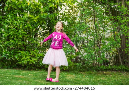 Adorable little girl spinning around in a beautiful park on a nice day, wearing tutu skirt, ballerina shoes and bright pink t-shirt