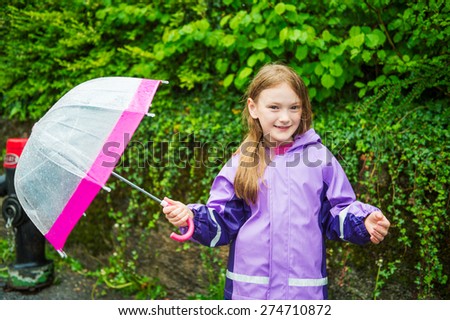 Pretty little girl under the rain, wearing purple rain coat, holding umbrella