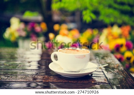 Empty cup of coffee with traces of lipstick on the table under the rain, outdoors, toned image