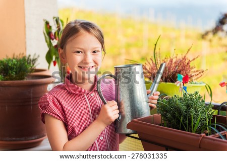 Adorable little girl watering plants on the balcony on a nice sunny day
