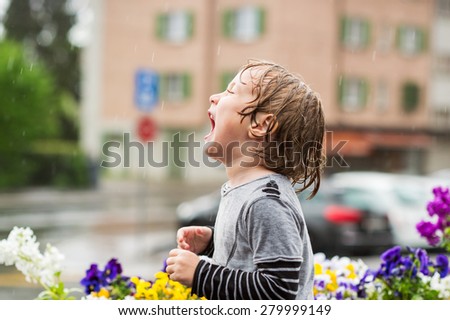 Cute little boy playing under the rain outdoors, catching rain drops by his mouth
