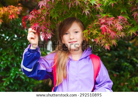Autumn portrait of adorable little girl wearing purple rain coat and red backpack