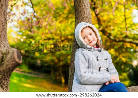 Autumn portrait of a cute little girl playing on a tree in a beautiful park on a nice sunny day