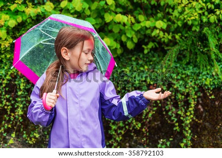 Pretty little girl under the rain, wearing purple rain coat, holding umbrella
