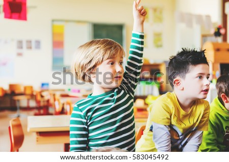 Two concentrated 4-5 year old boys in classroom, kid raising hand on lesson