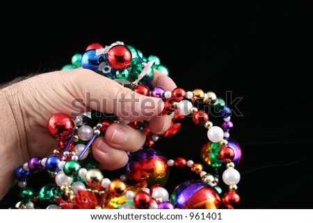 Hand holding Mardi Gras beads with black background.