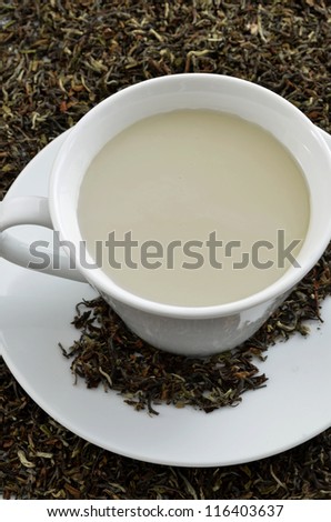 Black tea with milk standing on dried black tea leaves.
