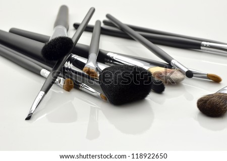 A bunch of make-up brushes lying randomly on white background with reflection.