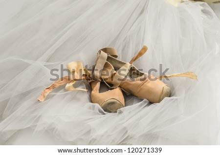 Old pointe shoes lying on a ballet dress.