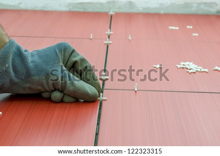 Closeup of handyman placing tile spacer between red ceramic tiles.