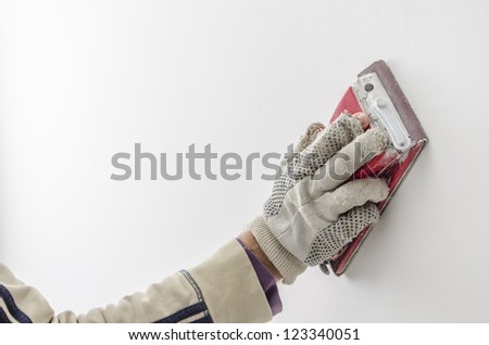 Closeup of a craftsman grinding a wall with sandpaper.