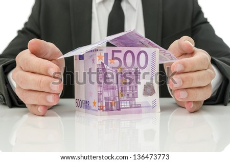 Male hands around money house as if they are giving it energy. Concept of real estate and insurance crisis solution.