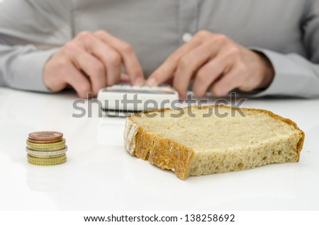 Bread slice and Euro coins on white desk with man calculating food costs in background.