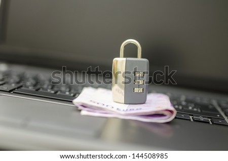 Padlock on money placed on laptop keyboard. Concept of safety of online banking.