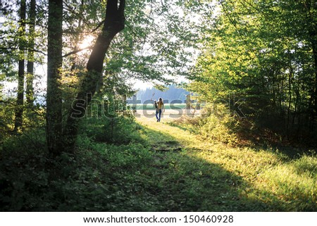 View from behind of mother and her toddler son walking in woods in early summer evening.