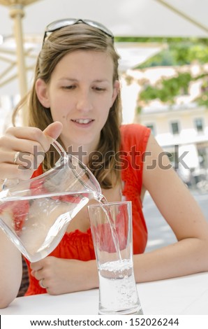Young woman sitting in restaurant pouring water into a glass.