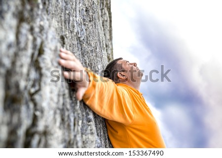 Young man leaning on rock of steep mountain climb with hands wide open.