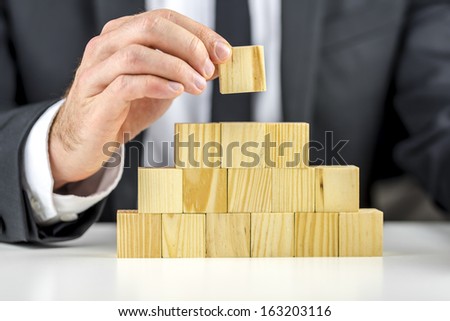 Closeup of businessman making a pyramid with empty wooden cubes. Concept of business hierarchy and human resources.