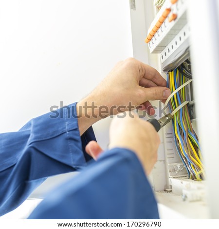 Electrician installing an electrical fuse box in a house working with pliers on the wiring circuits