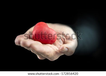 Man cupping a red heart in his hand as he offers it as a gift to a sweetheart symbolic of love and romance and a Valentines Day wish