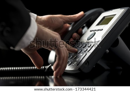 Low angle closeup view of the hands of a businessman in a suit dialing out on a telephone call using a dial-up desktop landline instrument as he presses the numbers on the keypad