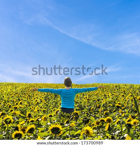 Young woman standing in the middle of sunflower field with arms wide open.