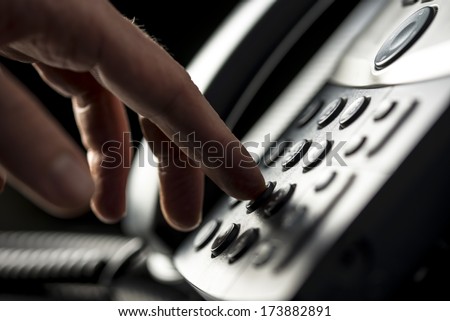 Closeup view of the hand of a man making a telephone call on a desktop instrument pressing the numbers on the keypad