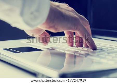 Closeup of the hands of a man typing on a laptop keyboard as he enters information or surfs the internet in an online communication and contact concept. With retro filter effect.