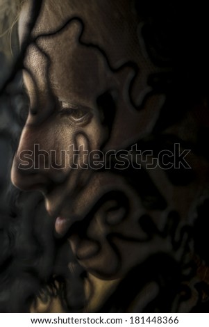 Evocative portrait of a woman in deep shadow throwing patterns across the side of her face with a serene thoughtful expression, close up of her profile.