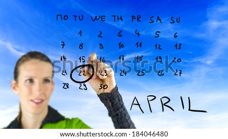 Woman marking Earth Day on a hand drawn calendar for the month of April on a virtual interface ringing the date of the 22nd raising awareness of conservation and the ecology.
