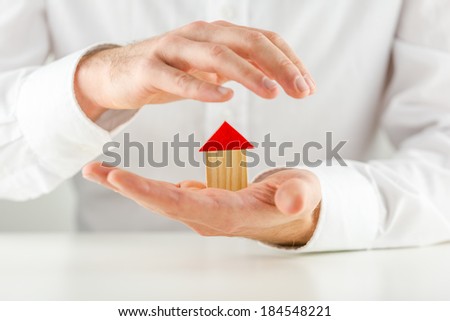 Man protecting a small wooden model house in his hands cupping it on his palm in a concept of ownership, investment, safety and security.