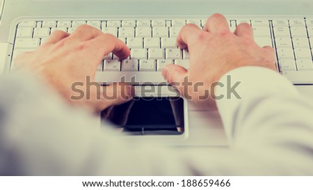 View from the mans perspective of his hands typing on a computer keyboard inputting information and data, toned retro or instagram effect.