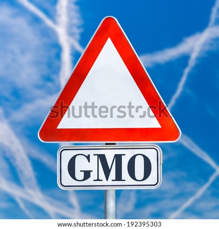 GMO, or genetically modified organism, white triangular traffic warning sign on a blue sky with jet contrails, conceptual image.