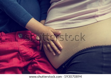 Retro image of child holding its mothers pregnant belly bonding with the unborn child in a show of love, closeup of the womans stomach and the hand of the youngster.