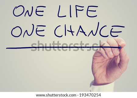 Retro instagram style image of a male hand writing phrase One life one chance on virtual screen.