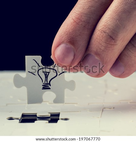Male hand inserting the final missing puzzle piece with light bulb drawn on it. Concept of innovation or getting a business idea.