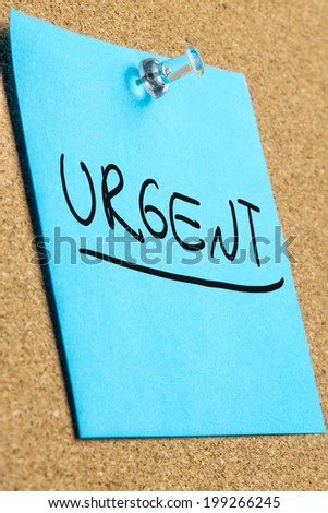 Blue post it paper pinned to a cork bulletin board with word Urgent written on it.