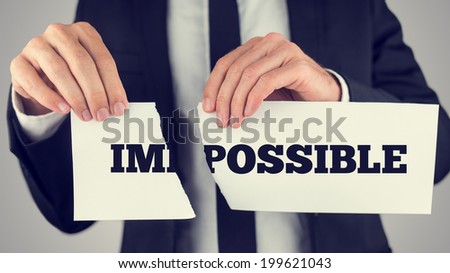 Businessman tearing up a sign saying - Impossible - conceptual of successfully overcoming problems and challenges and positive attitude , retro effect faded look.