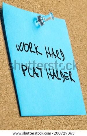 Idiom Work hard play harder written on blue post it paper pinned on cork bulletin board.
