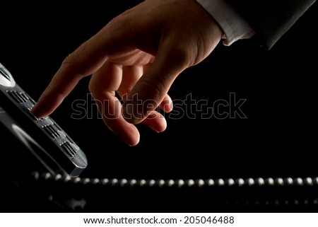 Close-up of the hand of a businessman dialing or initiating a phone call by operating the keypad of a desk corded land line telephone, on black.