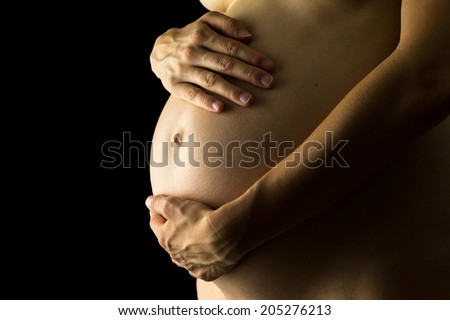 Shadowy portrait of the belly of a naked pregnant woman cradling her baby bump with her hands as she bonds with her unborn child , close up side view with copyspace.