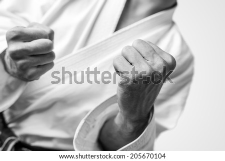 Black and white close up image of the bare fists of a man dressed for martial arts during training or in combat.