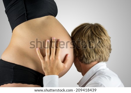 Man listening to the heartbeat of his unborn child with his head and ear pressed close against the swollen pregnant belly of his wife, side view looking away.