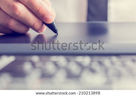 Retro image of male hand of a designer drawing with the stylus on a grey graphics tablet, close-up.