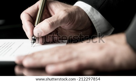Desaturated image of the hands of a businessman signing a contract with a fountain pen.